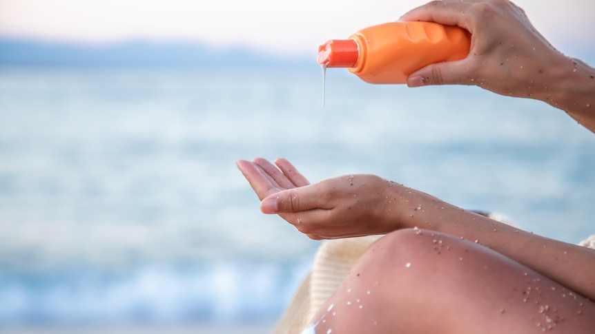 A person at the beach reapplying sunscreen 