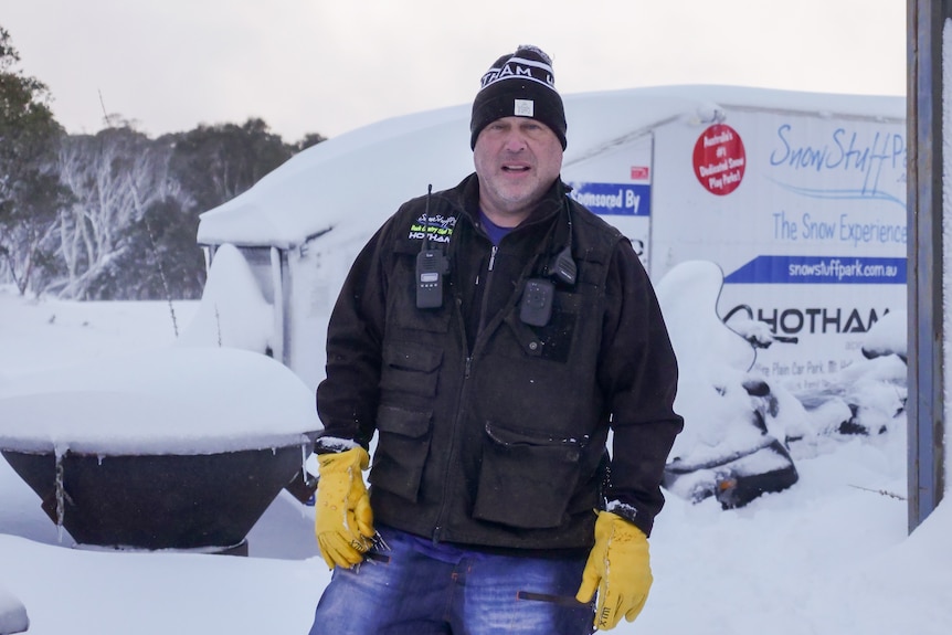 man in black vest with walkie talkie and yellow gloves in snow