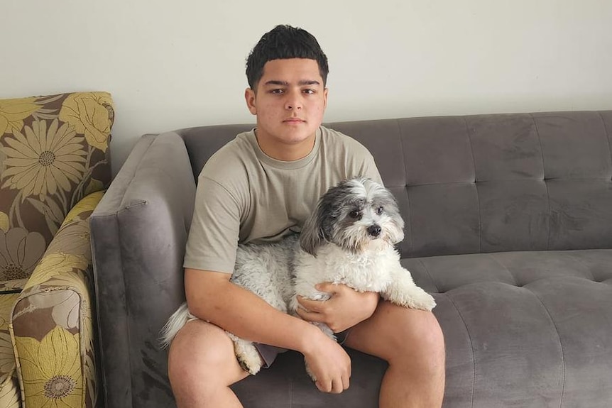 A teenage boy sits on a couch with a dog in his lap. 