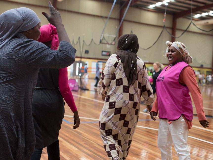 Entisar laughs as another woman waves her hand in the air during an indoor soccer match between Stand Up mums.