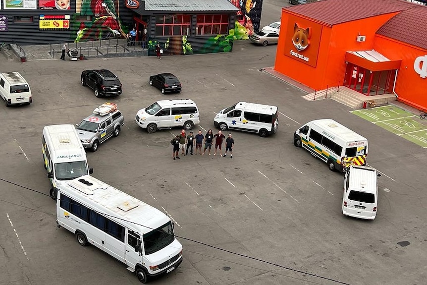 A collection of ambulances in a circle in a Ukraine car park with a group of people from Aus Ukraine Aid standing in the centre.