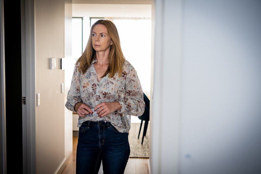 A woman walks down the hallway of her home wearing jeans and a top