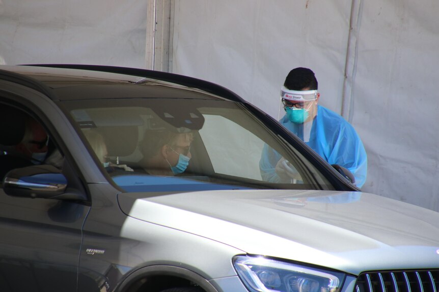 Medical worker speaks to people in a car at drive through COVID clinic.
