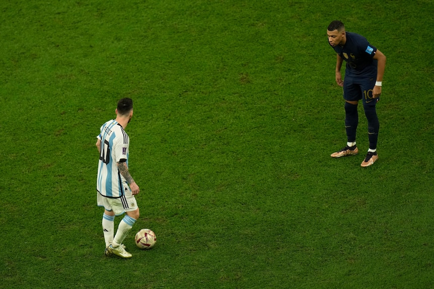 Two footballer from opposing teams stand metres apart on a green field.