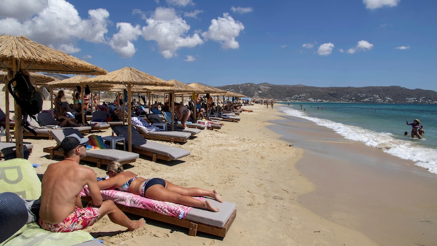 People sunbathe under a row of umbrellas at a beach on Greece. 