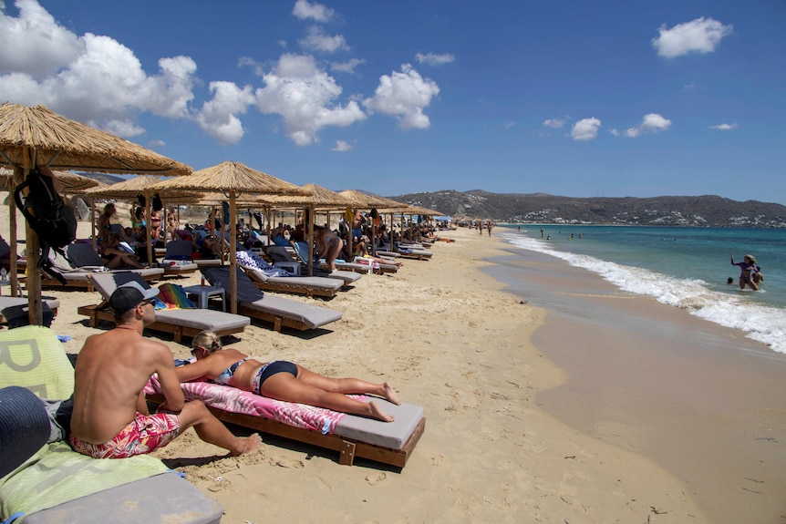 People sunbathe under a row of umbrellas at a beach on Greece. 