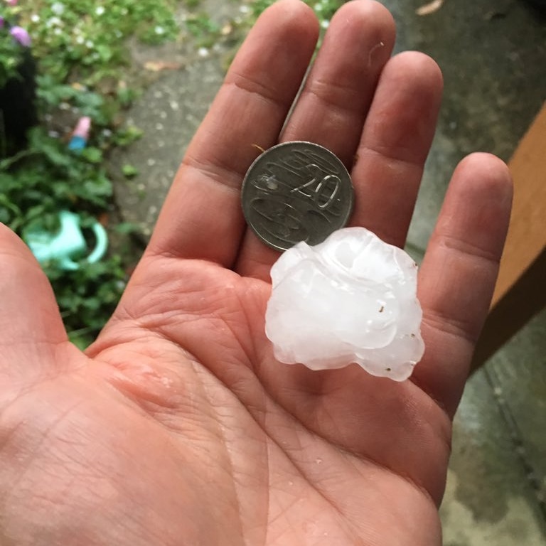 A man holds a hail stone next to a 20 cent coin.