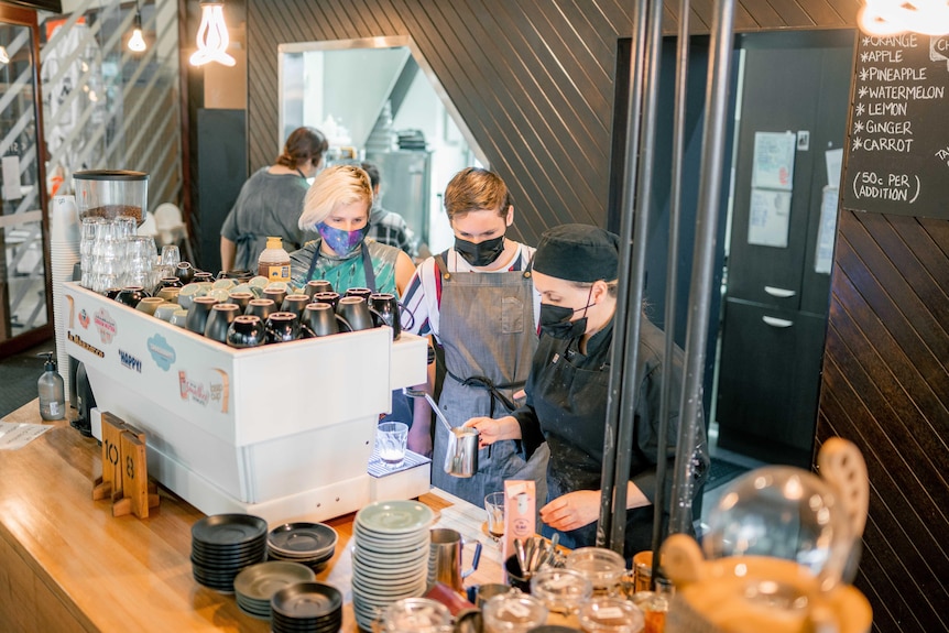 Two young people watching a hospitality worker make a coffee 