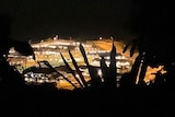 An aerial shot of the Christmas Island Detention Centre at night framed by the silhouettes of trees.