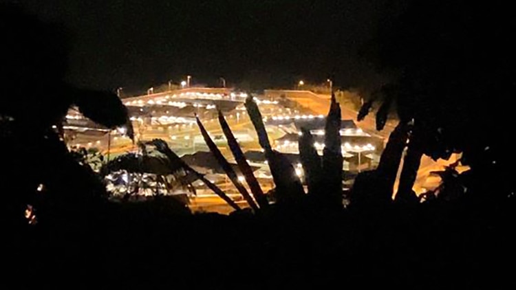 An aerial shot of the Christmas Island Detention Centre at night framed by the silhouettes of trees.