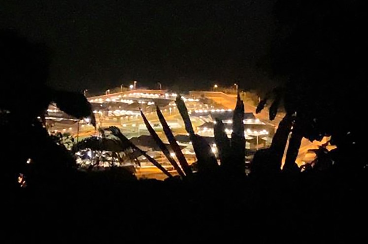 An aerial shot of the Christmas Island Detention Centre at night framed by the silhouettes of trees.