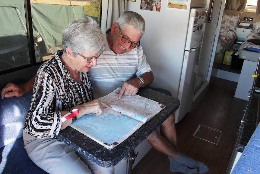An older couple look at a map book in their mobile home.
