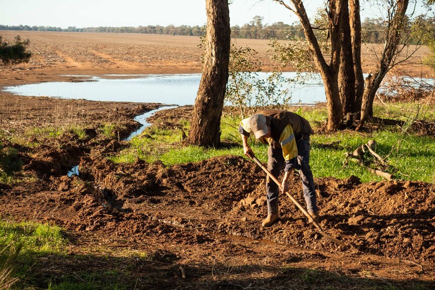 A man digs into the soil in front of a dam full of water.