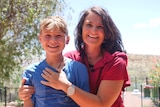 young boy in blue shirt and woman with brown hair and red shirt in front of ranges