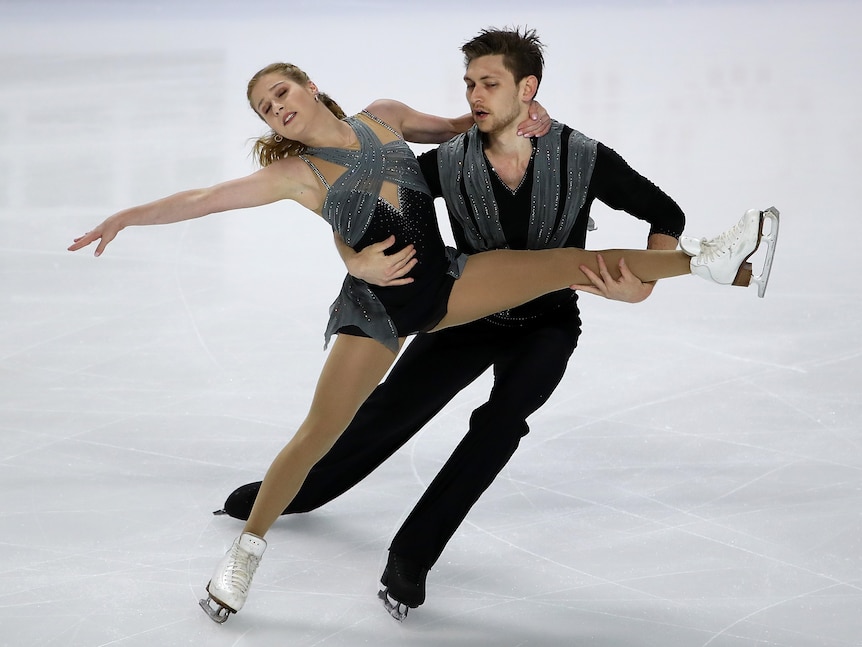 A female figure skater closes her eyes in mid-routine on the ice as her male partner holds her by the leg and waist.