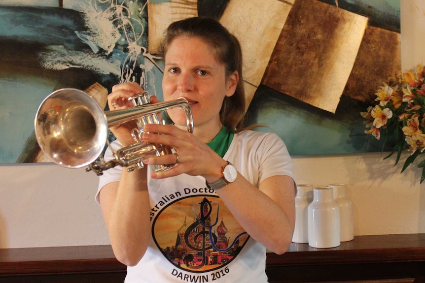Woman wearing a t-shirt playing a trumpet and standing in a lounge room of a house