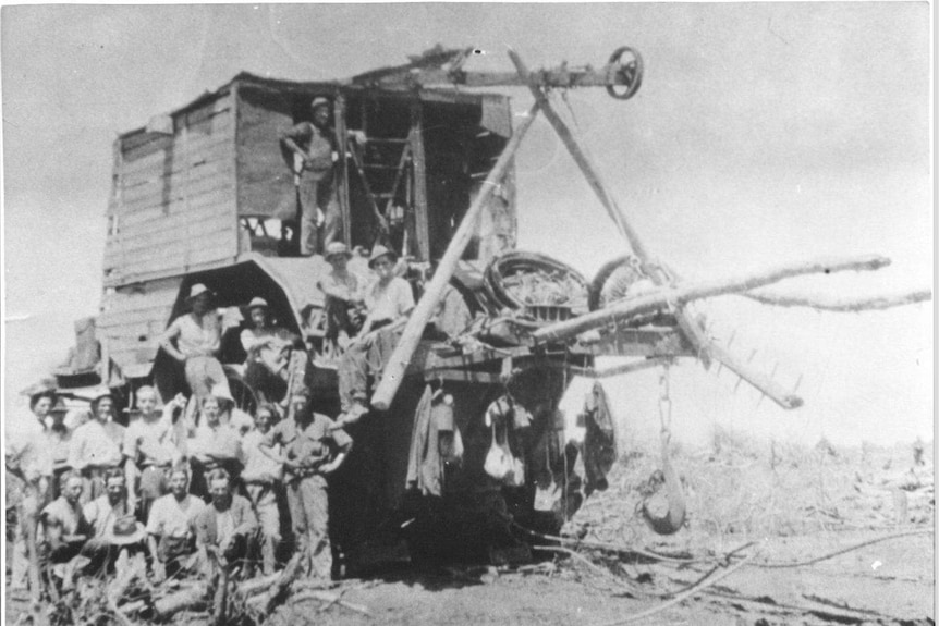 Black and white photo of giant tractor with gang of men