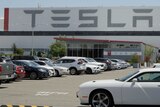 A parking lot outside a large warehouse building with TESLA signs