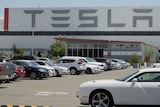 A parking lot outside a large warehouse building with TESLA signs