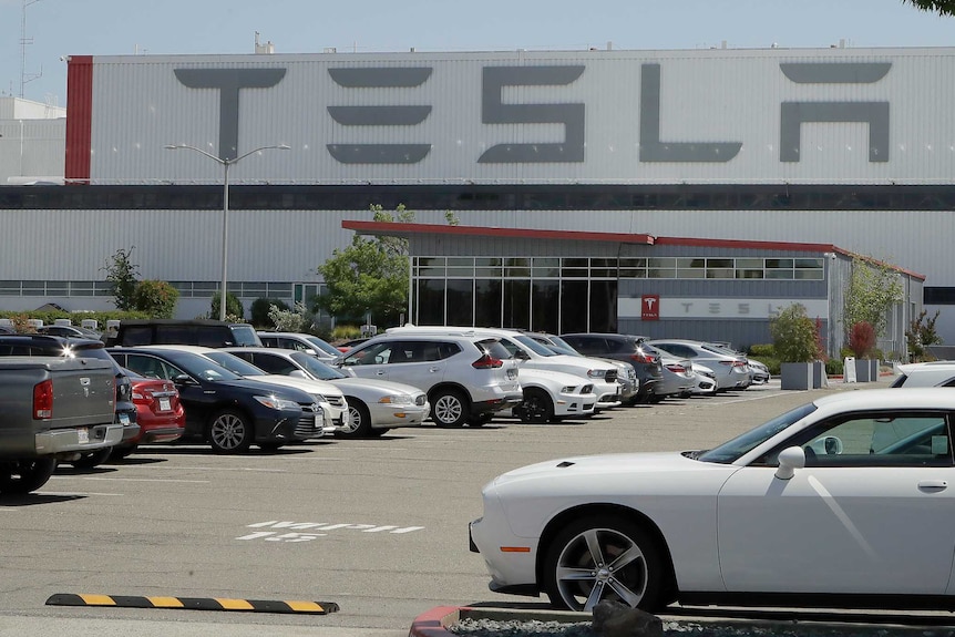 A parking lot outside a large warehouse building with TESLA signs