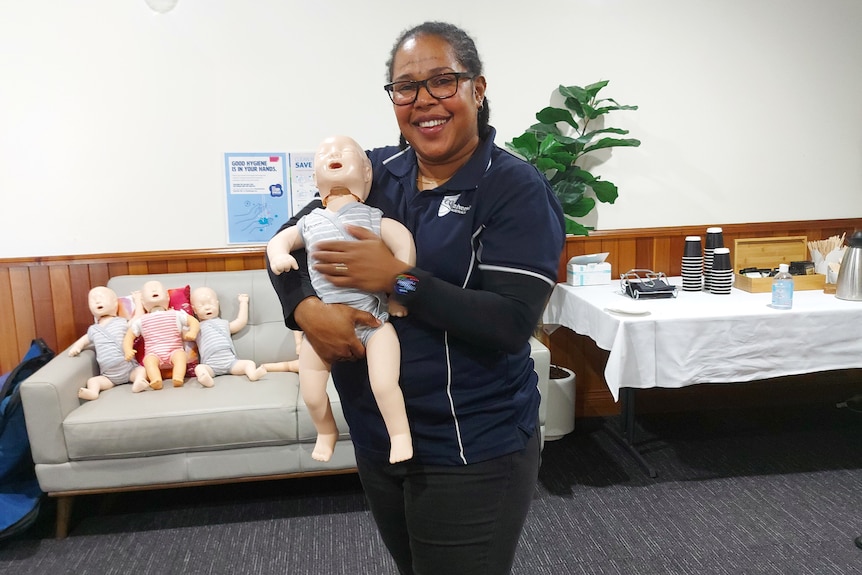 Sophie holding a child mannequin, others in the background on a couch. 