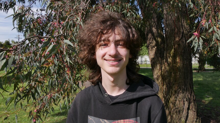 Young man smiling in front of gum tree.