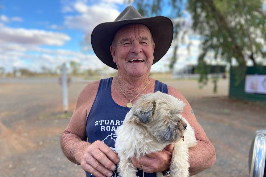 A man smiles while holding a small white dog