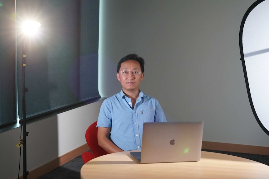 a man sitting in front of lights with a laptop on a table