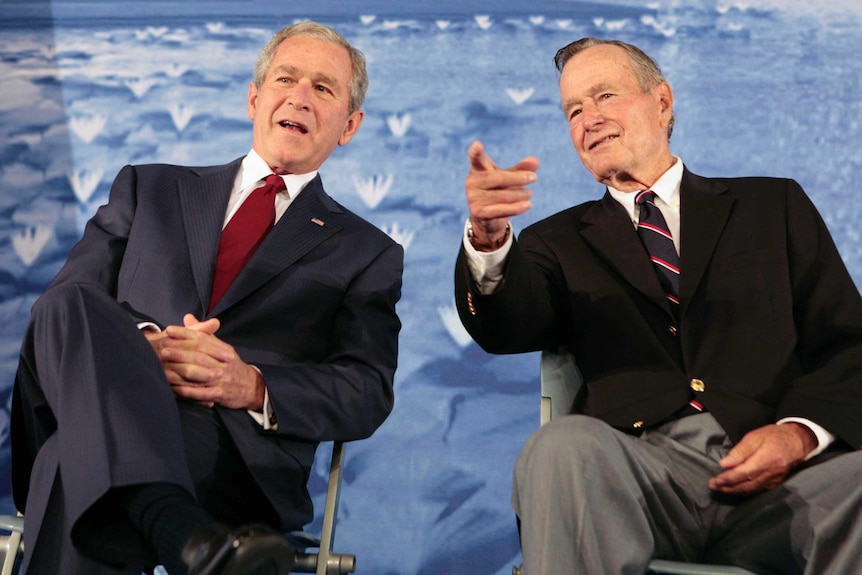 George W Bush and George HW Bush sitting together, both wearing suits.
