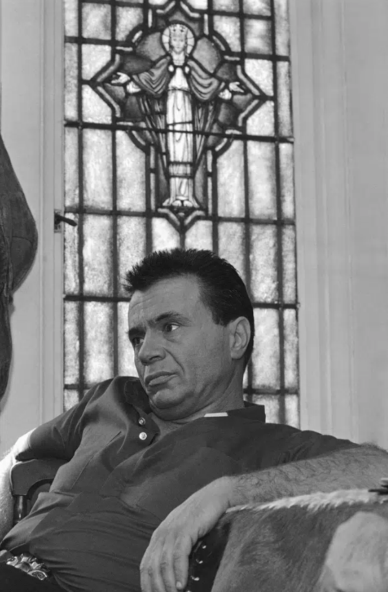 A black and white photo of actor Robert Blake sitting on a couch, posing 