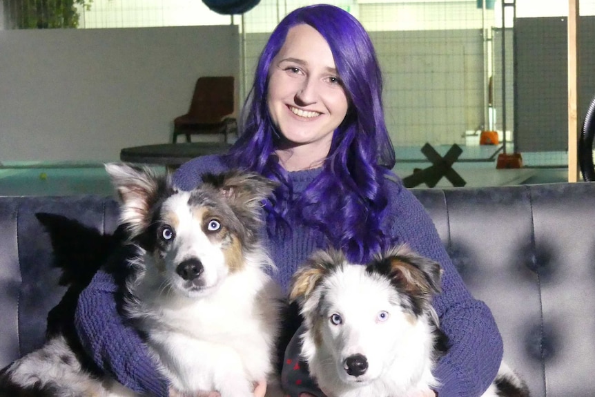 Maddie Johnson with sits with two dogs on a couch.