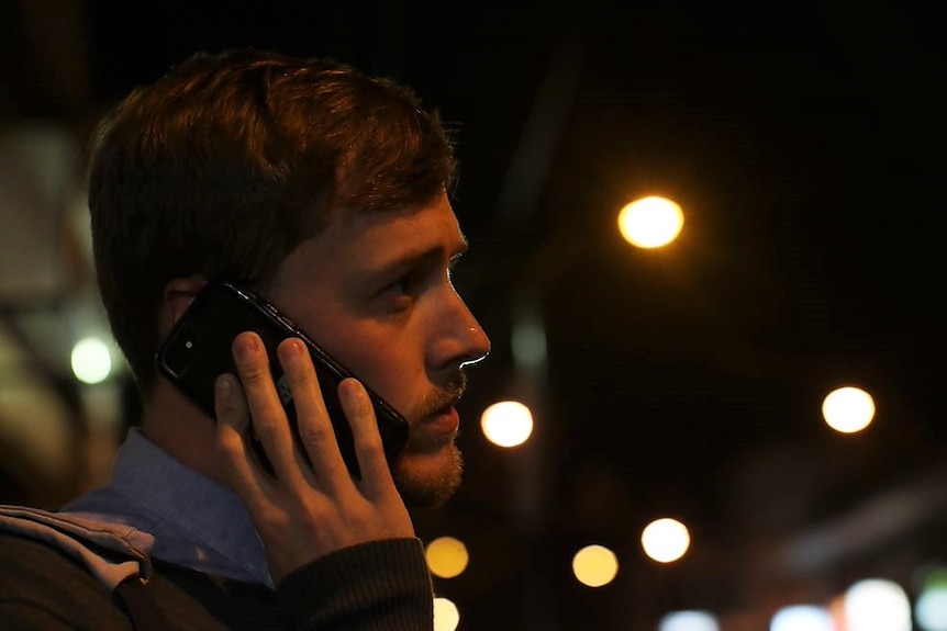 Psychiatric nurse Chris Ward makes a phone call while standing on a city street at night. He looks concerned.