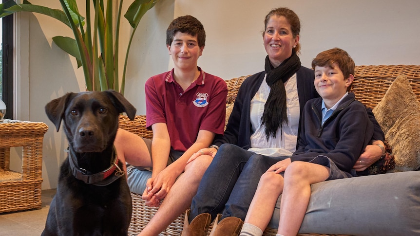 A mother sitting on a cane couch with her two sons and a dog