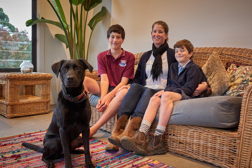 A mother sitting on a cane couch with her two sons and a dog