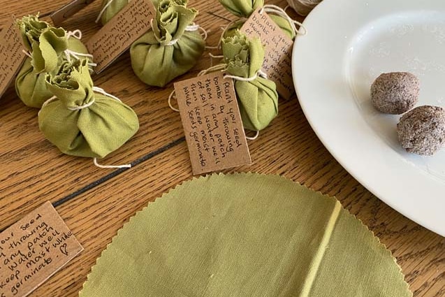 Balls of seeds on a plate, some wrapped in pieces of fabric, adorned with cardboard labels.