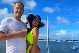 A man in a white shirt stands with a woman in a yellow swimsuit on a boat.