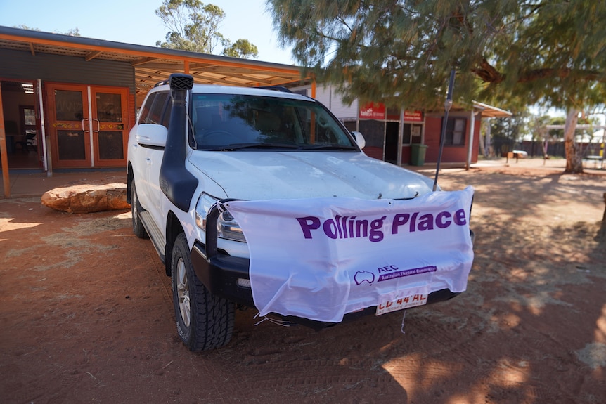 A car parked out the front of a building, with a banner reading 'polling place' on it