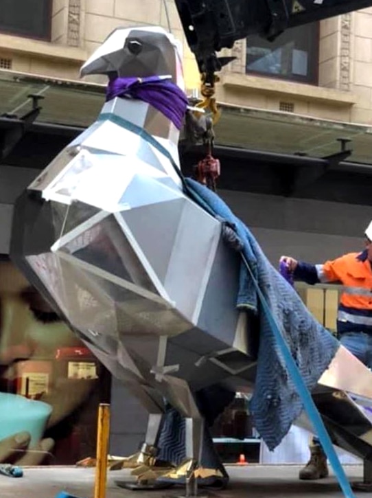 A giant steel pigeon is installed in a mall by a workman.