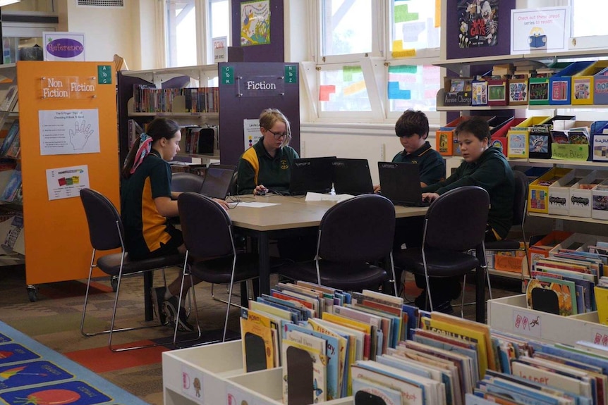 Two boys and two girls sitting at a table with laptops in a library.