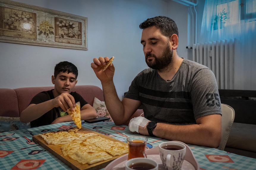 Un uomo e un ragazzo seduti a un tavolo che condividono un piatto di focaccia.  C'è anche un vassoio con tazze di tè sul tavolo