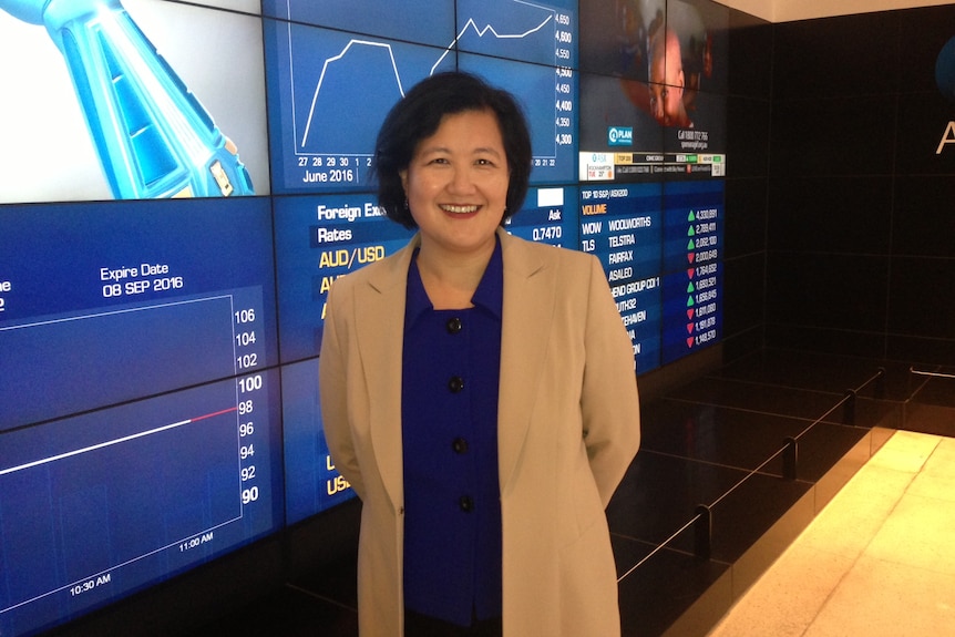 Ming Long standing in front of plasma screens displaying stocks.