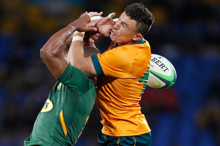 A Wallabies player attempts to catch a high ball while in an aerial contest with a Springboks opponent.
