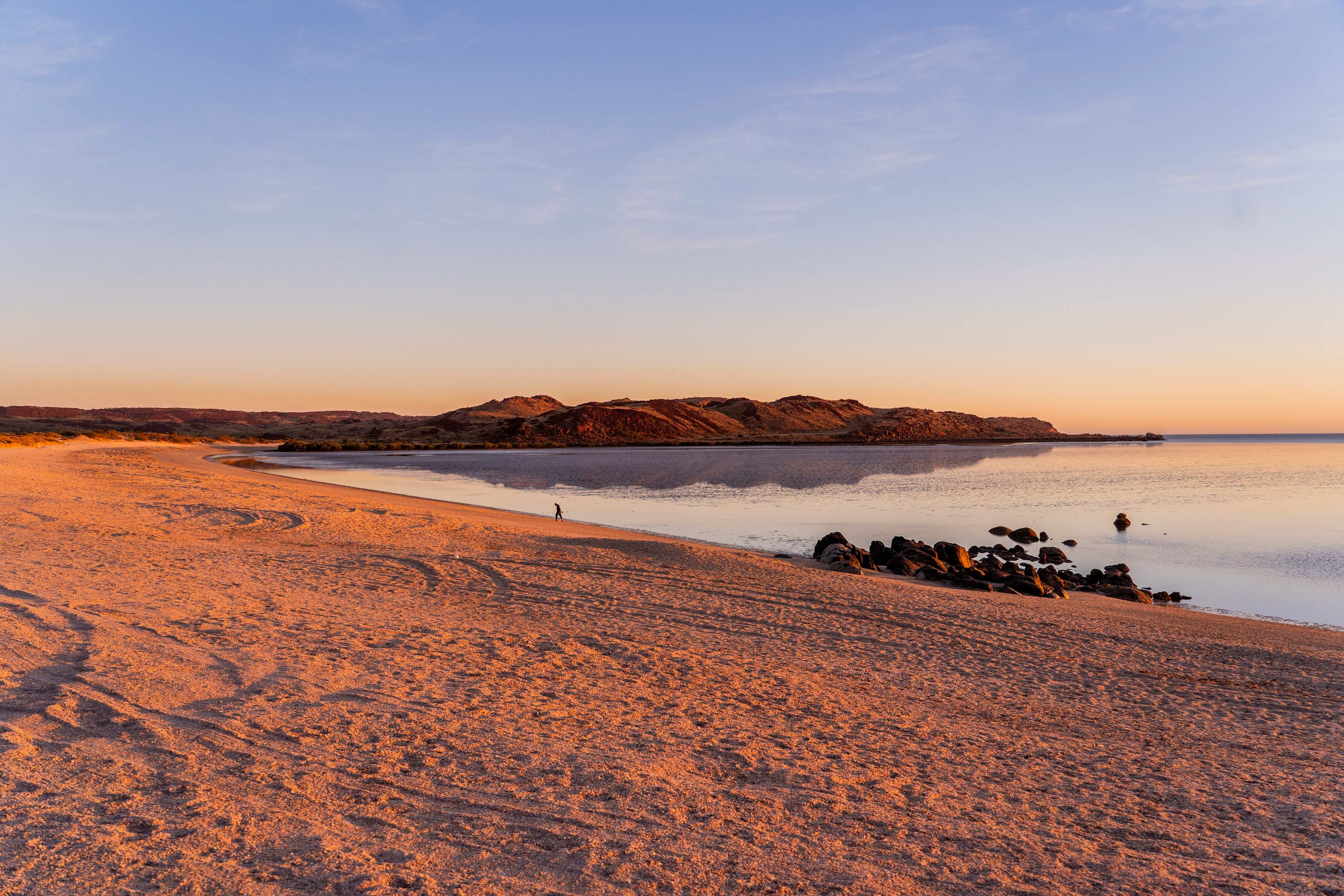 Um pôr do sol em uma praia de areia laranja e uma colina ao fundo.