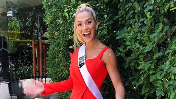 A woman with blonde hair in a red dress and a sash that reads 'USA' poses for the camera.