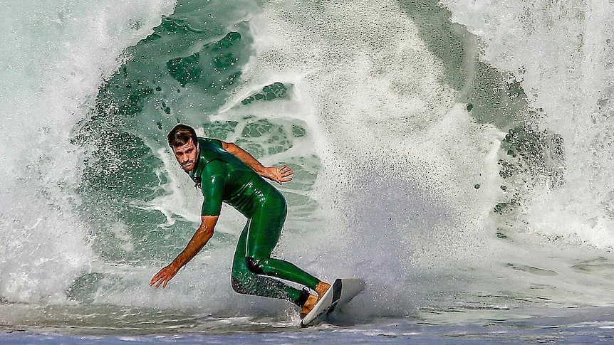 A surfer in a green wetsuit in front of a green wave