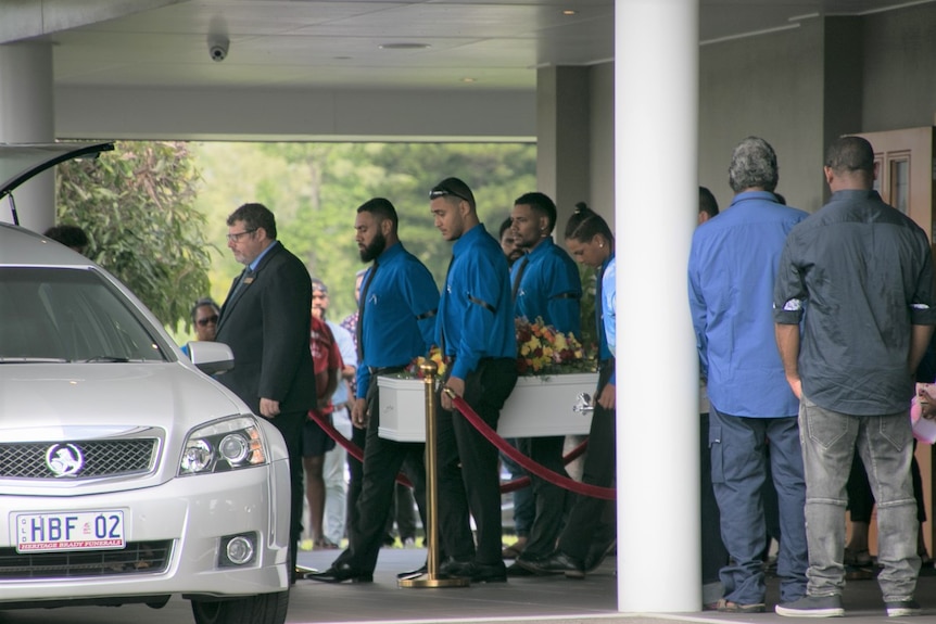 Pallbearers wearing blue carrying coffin