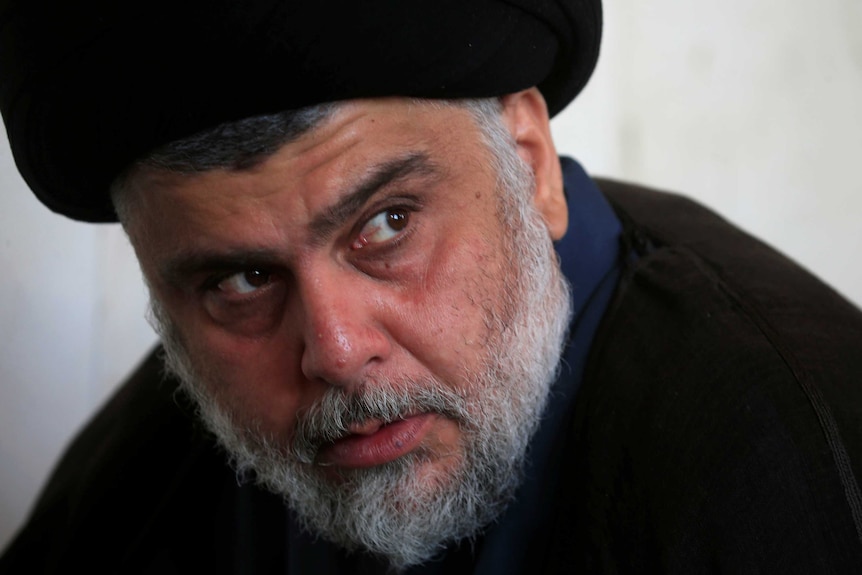 Muqtada al-Sadr is pictured close-up, looking into the distance as he wears black robes and a headpiece.