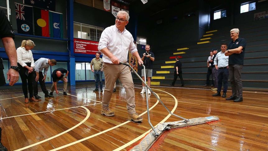 PM Scott Morrison mops a flooded basketball court in Brisbane.