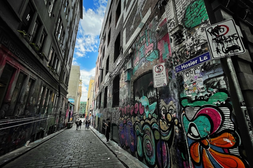 Graffiti across walls of Hosier Lane in Melbourne, people seen to the distance.