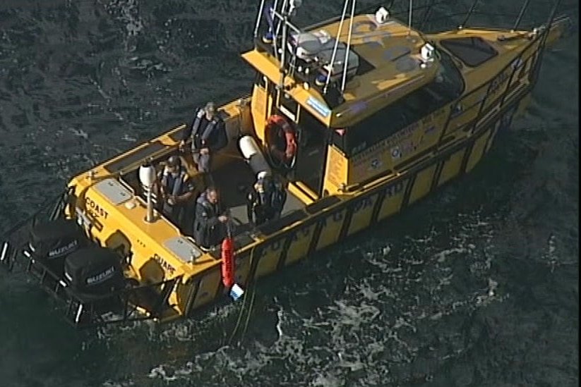 A man on a Coast Guard vessel retrieves a buoy and diver flag from Port Phillip Bay.